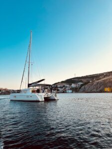 A serene sailboat cruises in Bozcaada Harbor at sunset, showcasing stunning coastal scenery.