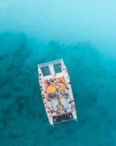 Drone captures catamaran with tourists in crystal clear turquoise water. Perfect travel scenery.